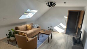 A modern loft apartment with a sloped ceiling, a sofa, a chair, a coffee table, and a TV stand. - Cozy DG vacation apartment with balcony for 1 - 5 persons (Neustadt bei Coburg)