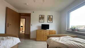 A bedroom with two beds, a TV on a wooden cabinet, and a window with a view. - Cozy DG vacation apartment with balcony for 1 - 5 persons (Neustadt bei Coburg)