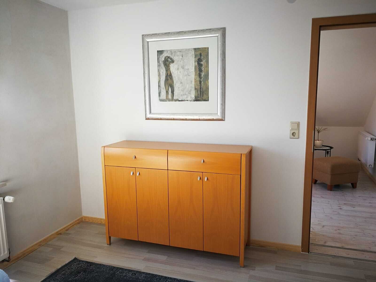 Une pièce avec un meuble en bois, une œuvre d’art encadrée accrochée au mur et une porte donnant sur une autre pièce.