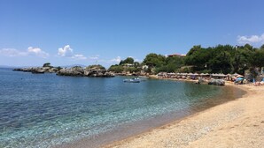 A beach with clear water, a rocky outcrop, and a row of beach umbrellas. - Our beautiful Greek home with private pool, large outdoor areas and lovely views (Stoupa)
