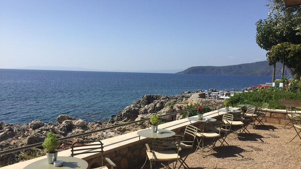 An outdoor seating area with tables and chairs overlooking a rocky coastline and the sea. - Our beautiful Greek home with private pool, large outdoor areas and lovely views (Stoupa)
