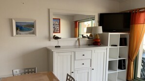 Een kamer met een wit kastje, een televisie en een ingelijste foto aan de muur.