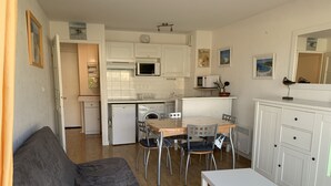 Een compacte woonruimte met een kitchenette, een eethoek met tafel en stoelen, en een bank.