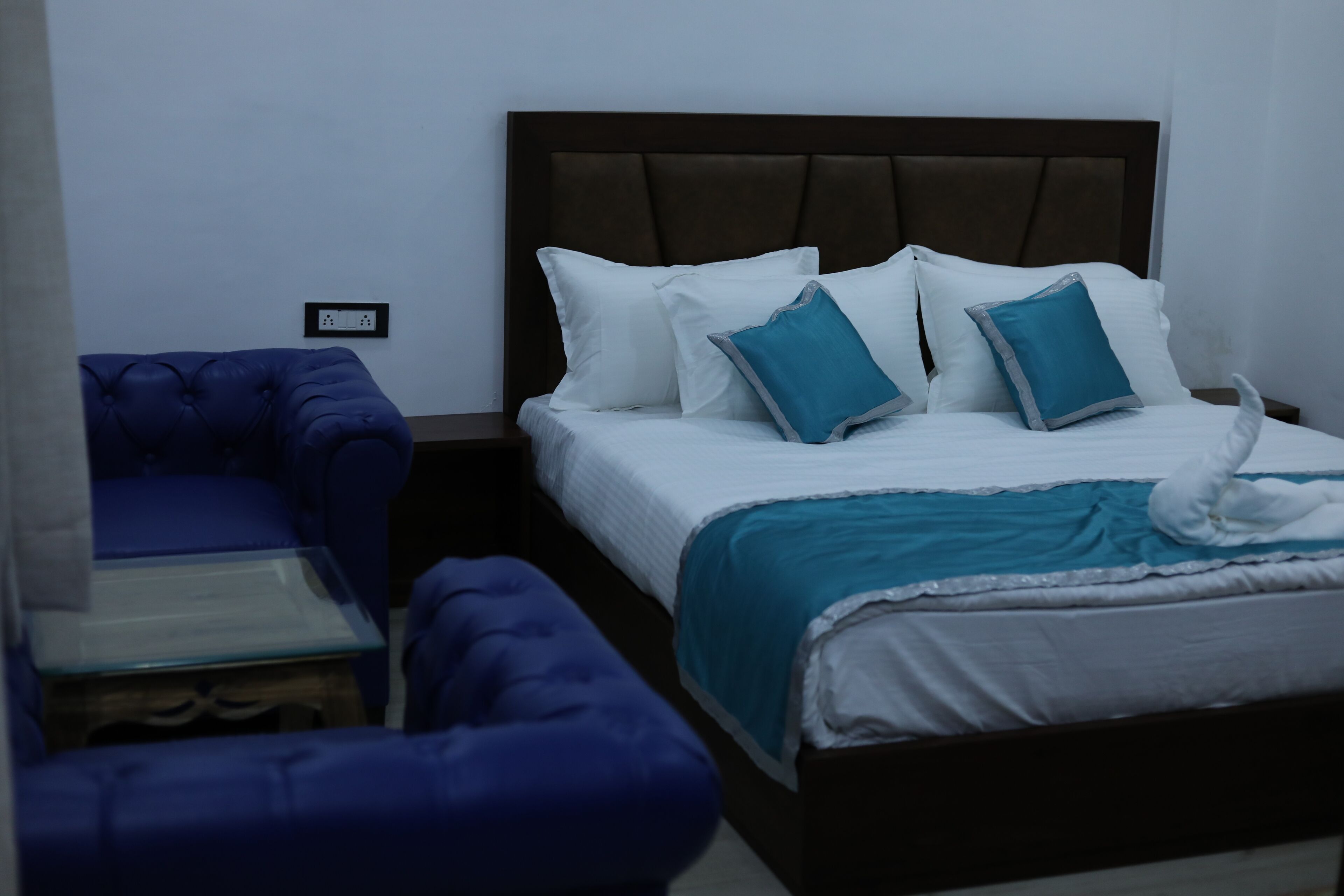 A hotel room with a bed, a blue armchair, and a small table.