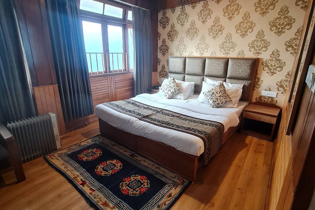 A bedroom with a large bed, a headboard, a nightstand, a radiator, a window with curtains, and a patterned rug.