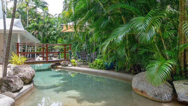 Ein tropischer Garten mit klarem Pool, umgeben von Felsen und Palmen.