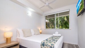 Ein Schlafzimmer mit einem Bett, einem Nachttisch, einer Lampe, einem Deckenventilator und einem Fenster mit Blick auf Grünflächen.