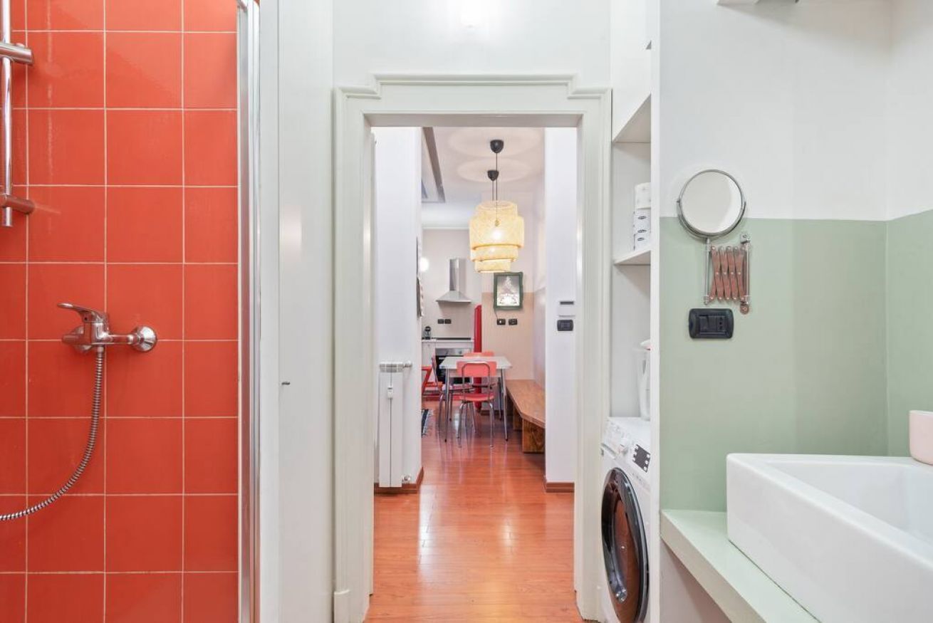A hallway with a shower, a washing machine, and a dining area with chairs and a table.