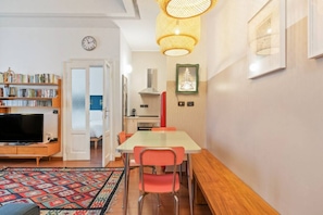 A compact living space with a dining area, a television, a bookshelf, and a kitchen area.