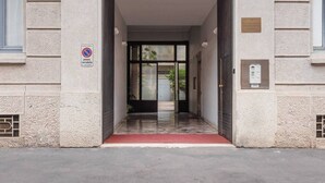 Entrada de un edificio con un cartel de no estacionamiento, alfombra roja y puerta de vidrio que da al interior.