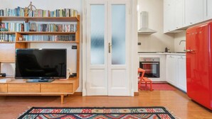 Una sala de estar con televisor, estantería y puerta que da a una cocina.