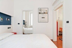 A bedroom with a bed, a framed picture on the wall, and a door leading to another room.