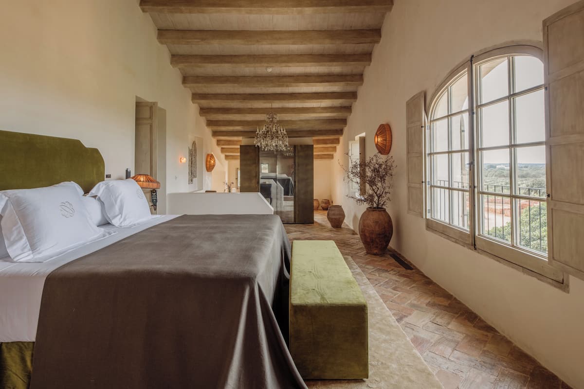 Un dormitorio con cama, banco, ventana grande y vistas al exterior.