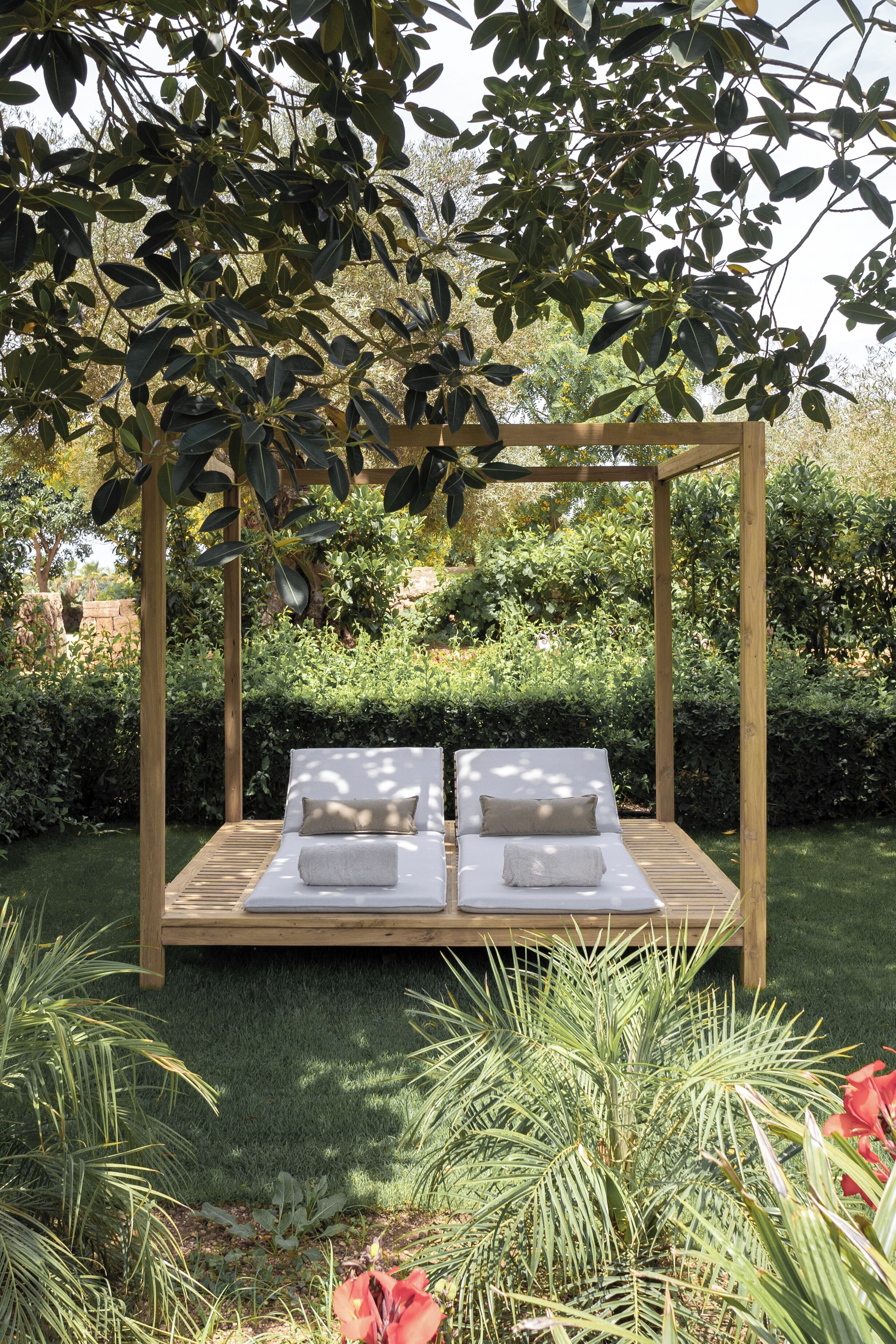 A wooden swing bed with white cushions in a garden setting.