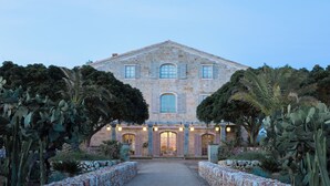 A large stone building with a symmetrical facade, multiple windows with shutters, and a central entrance.