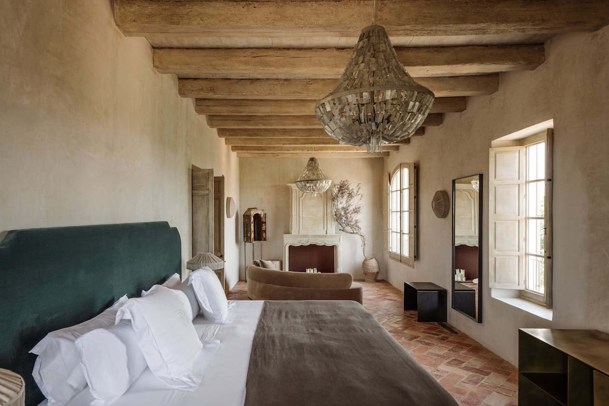 Un dormitorio con una cama grande, techo de madera, candelabro y chimenea.