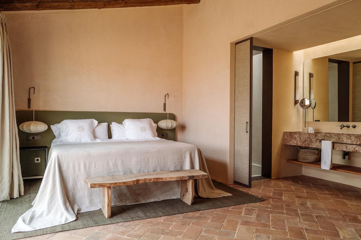 Un dormitorio con cama, mesita de noche y baño con espejo y lavabo.