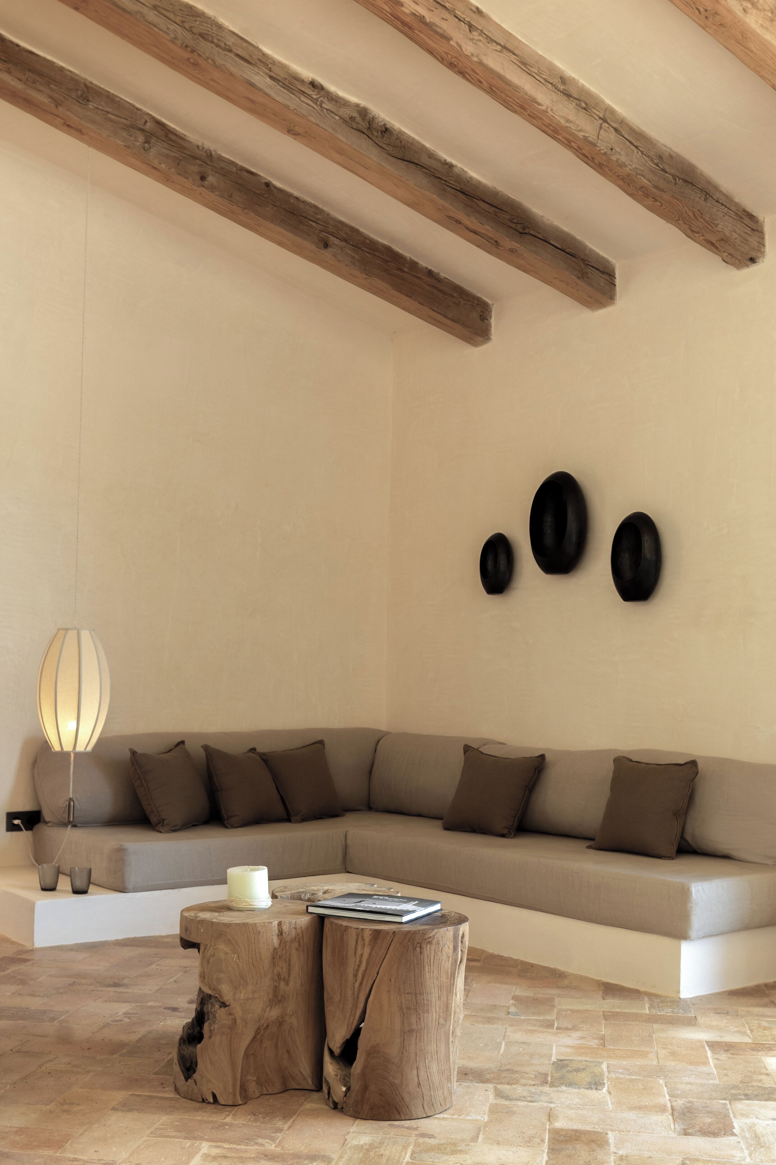 Uma sala de estar moderna com um sofá seccional, vigas de madeira, uma mesa de centro redonda e um luminário fixado na parede.