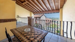 A balcony with a tiled table and chairs, a view of buildings, and a wooden ceiling.