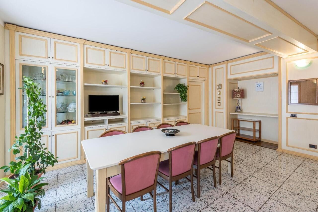 Zona pranzo con tavolo bianco e sedie rosa, circondata da mobili contenitori in legno con vetrine.