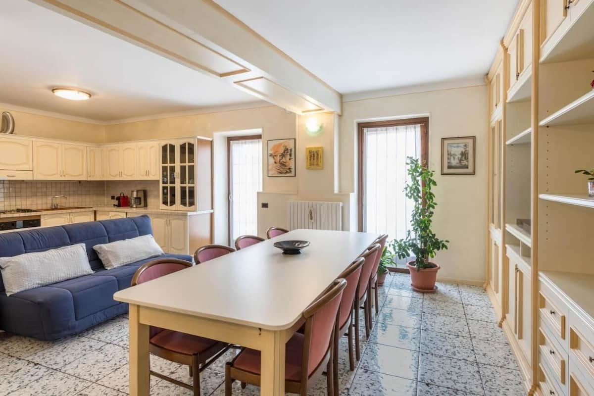 A compact kitchen with a dining table, chairs, a sofa, and a potted plant.