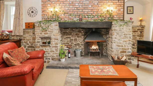 Una sala de estar acogedora con chimenea de piedra, un sofá de cuero rojo, una mesa de centro de madera y un televisor.