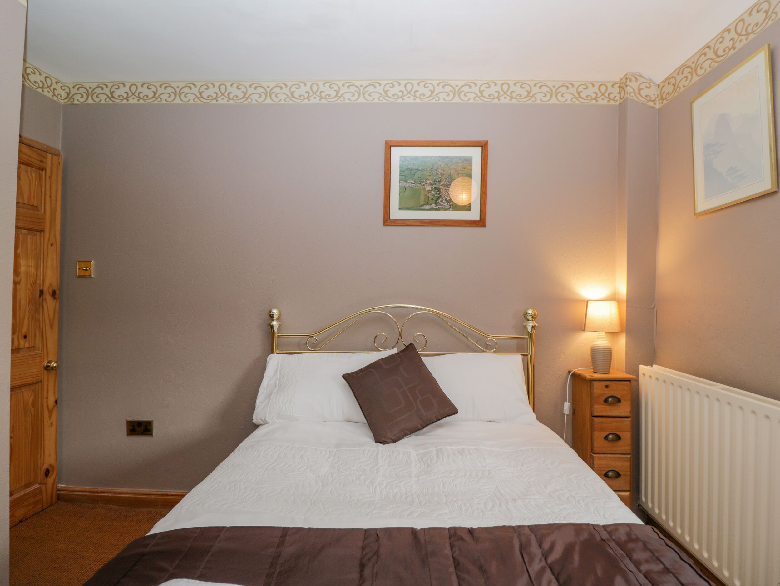 A bedroom with a bed, a nightstand, a radiator, a door, and a framed picture on the wall.