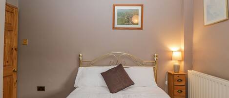 A bedroom with a bed, a nightstand, a radiator, a door, and a framed picture on the wall.