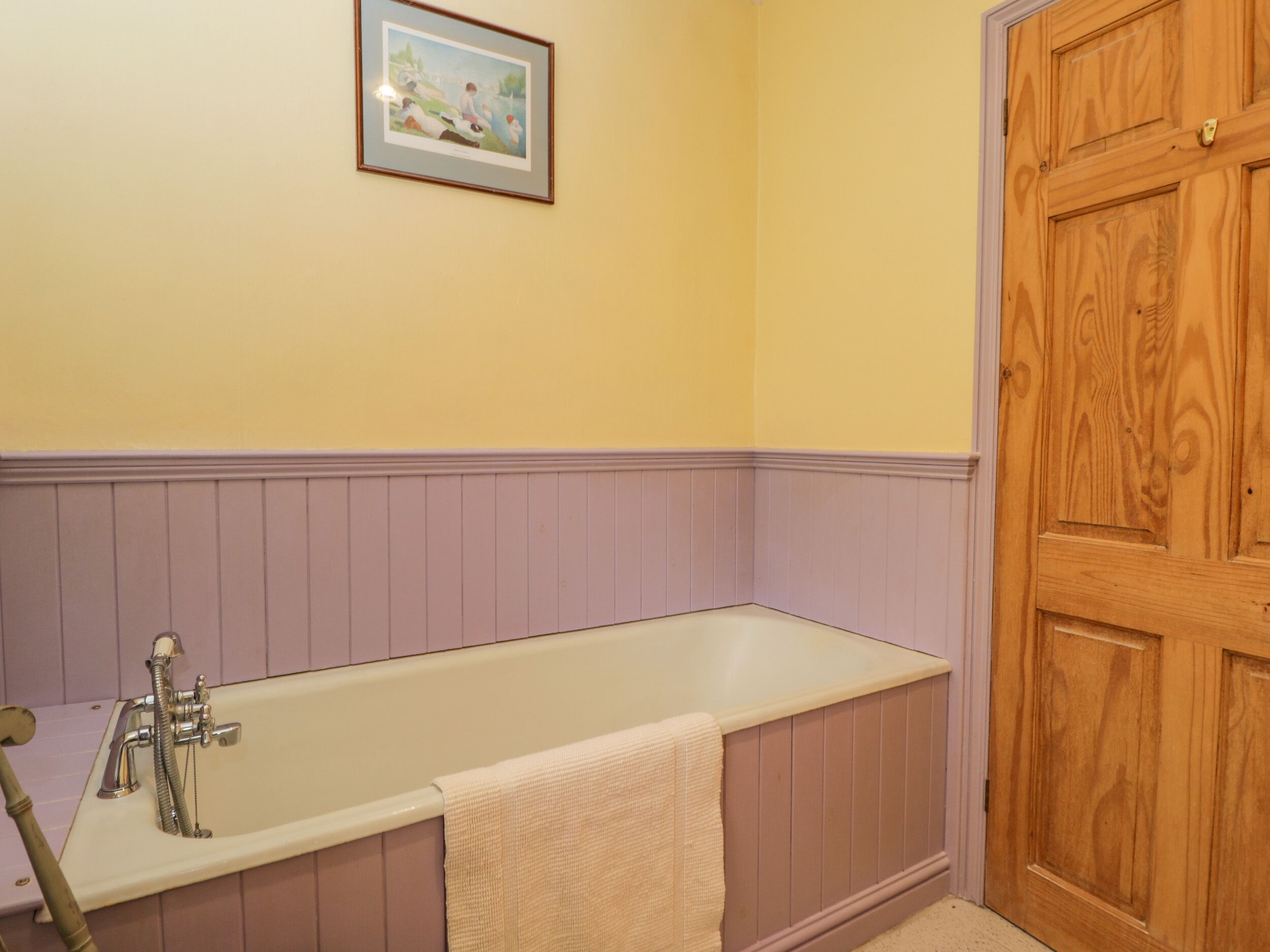 Ein Badezimmer mit einer Badewanne, einer Holztür und einem gerahmten Bild an der Wand.