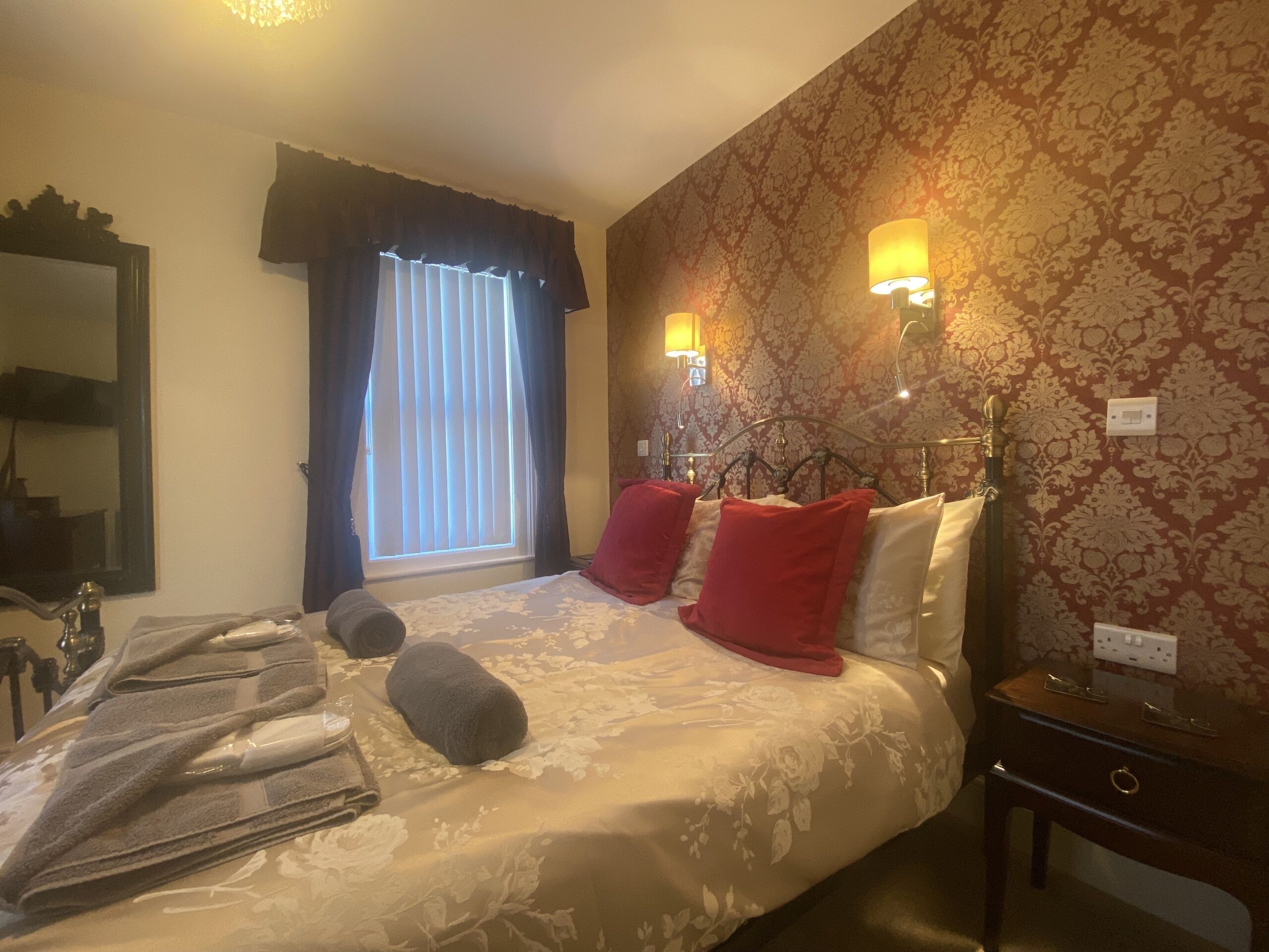 Habitación de hotel con cama, toallas, mesita de noche, espejo y ventana con cortinas.