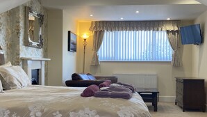 A bedroom with a large bed, a fireplace, a window with curtains, a desk, and a dresser. - The Beach House Luxury Rooms (Weston-super-Mare)