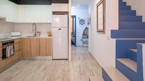 A modern kitchen with wooden cabinets, a white refrigerator, and a built-in oven. A staircase with blue steps leads to a landing with a decorative wall piece. - Charming Fisherman's House, 150m from Beach, A/C, WiFi, 3 Bedrooms, Central Palamós (Palamós)