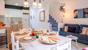 A modern living room with a dining area, featuring a blue sofa, a small round table, and a staircase leading to an upper level. - Charming Fisherman's House, 150m from Beach, A/C, WiFi, 3 Bedrooms, Central Palamós (Palamós)