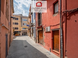 A narrow street with buildings on either side, a sign for 'Integral Finques', and a clear sky.