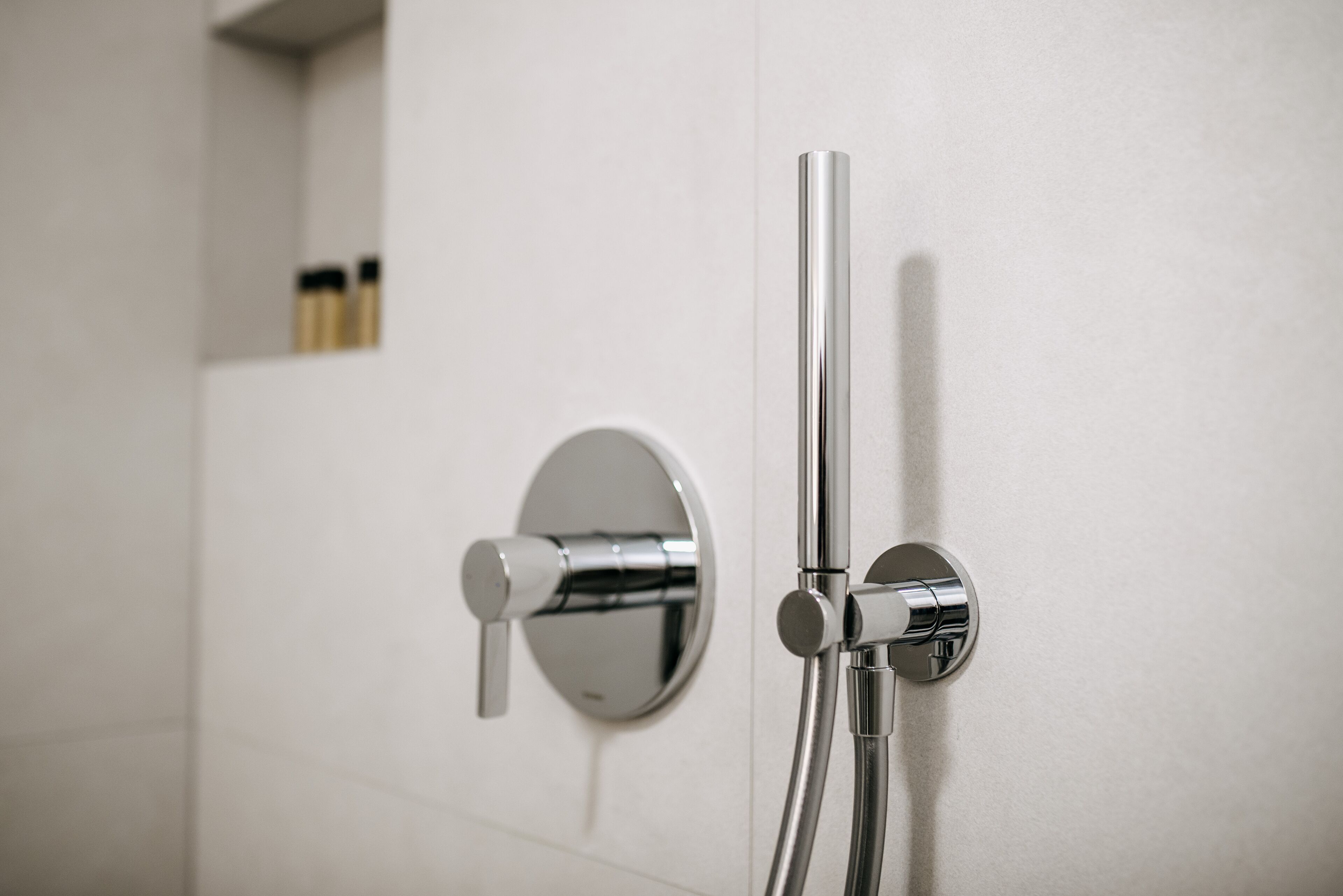 A modern bathroom with a chrome shower head and control knobs mounted on a white wall.
