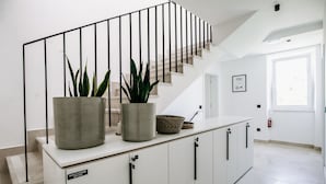 A staircase with a metal railing, a white wall, and a white floor. There are two potted plants on the landing.