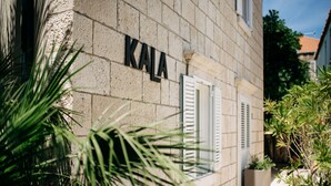A building with the name "KALA" on a stone wall, a window with shutters, and potted plants.