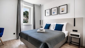 A modern bedroom with a large bed, a bedside table, a chair, and a window with curtains.