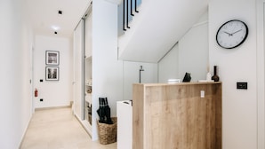 Un pasillo moderno con un mostrador de recepción de madera, un reloj en la pared y una escalera con diseño geométrico.