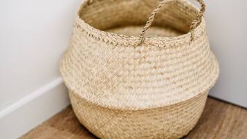 A woven basket with handles placed on a wooden surface against a white wall.