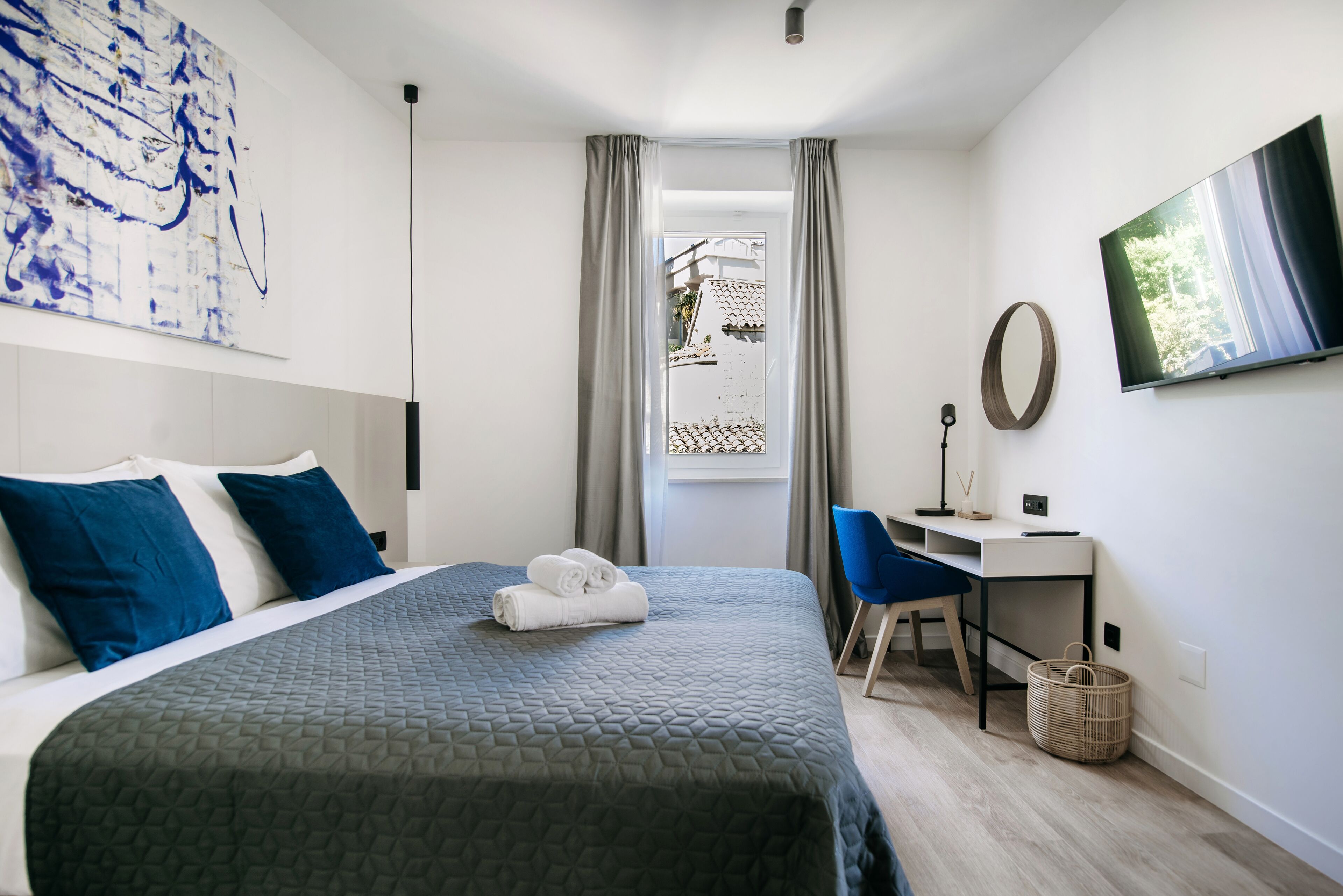 A hotel room with a bed, a desk, a chair, a TV, and a window with curtains.