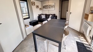 A modern living room with a dark wooden table, white chairs, a black sofa with cushions, and a large painting on the wall. - Cozy Chalet for 6 with Heated Pool, Terrace & Parking, Near Beach (Jullouville)