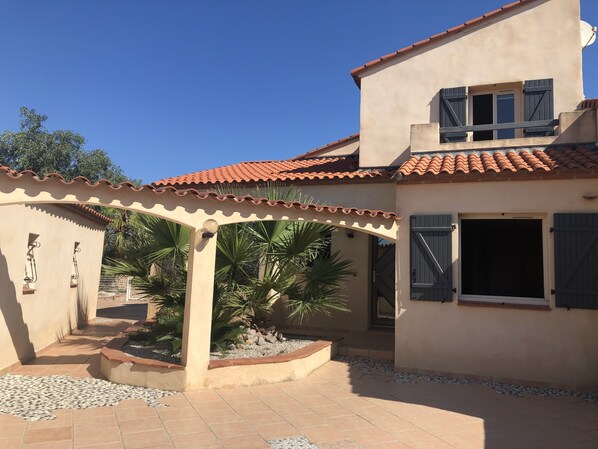 Une maison avec un toit en tuiles, un patio couvert et un jardin agrémenté de palmiers.