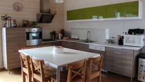 Een moderne keuken met een witte tafel, houten stoelen, een inbouwoven en een groene achterwand.