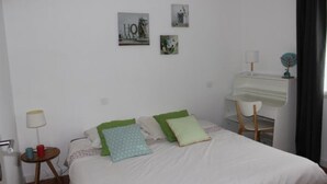 Een slaapkamer met een bed, kussens, een bureau, een stoel, een lamp en wanddecoratie.