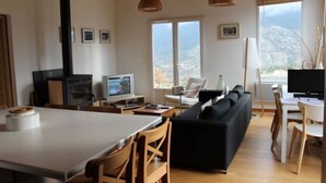 Een moderne woonkamer met een zwarte bank, een houten eettafel en stoelen. Er is een televisie en een open haard.