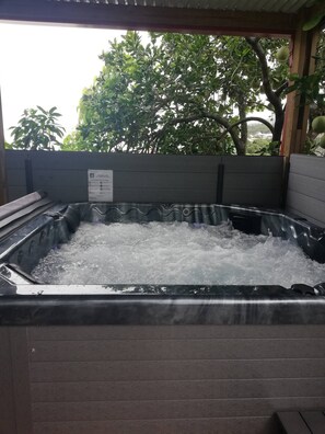 A hot tub filled with water, surrounded by a wooden deck and a metal railing. - 3* meublě de tourisme (Saint-Joseph)
