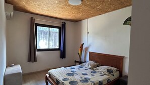 Ein Schlafzimmer mit Holzboden, einem Bett mit gemustertem Überwurf, einem Nachttisch mit einer Vase und einem Fenster mit Vorhängen.