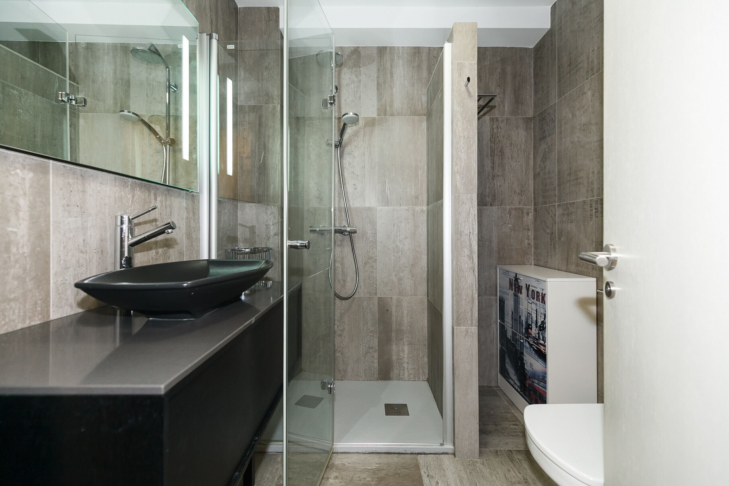 A modern bathroom with a glass-enclosed shower, a black sink, and a toilet.