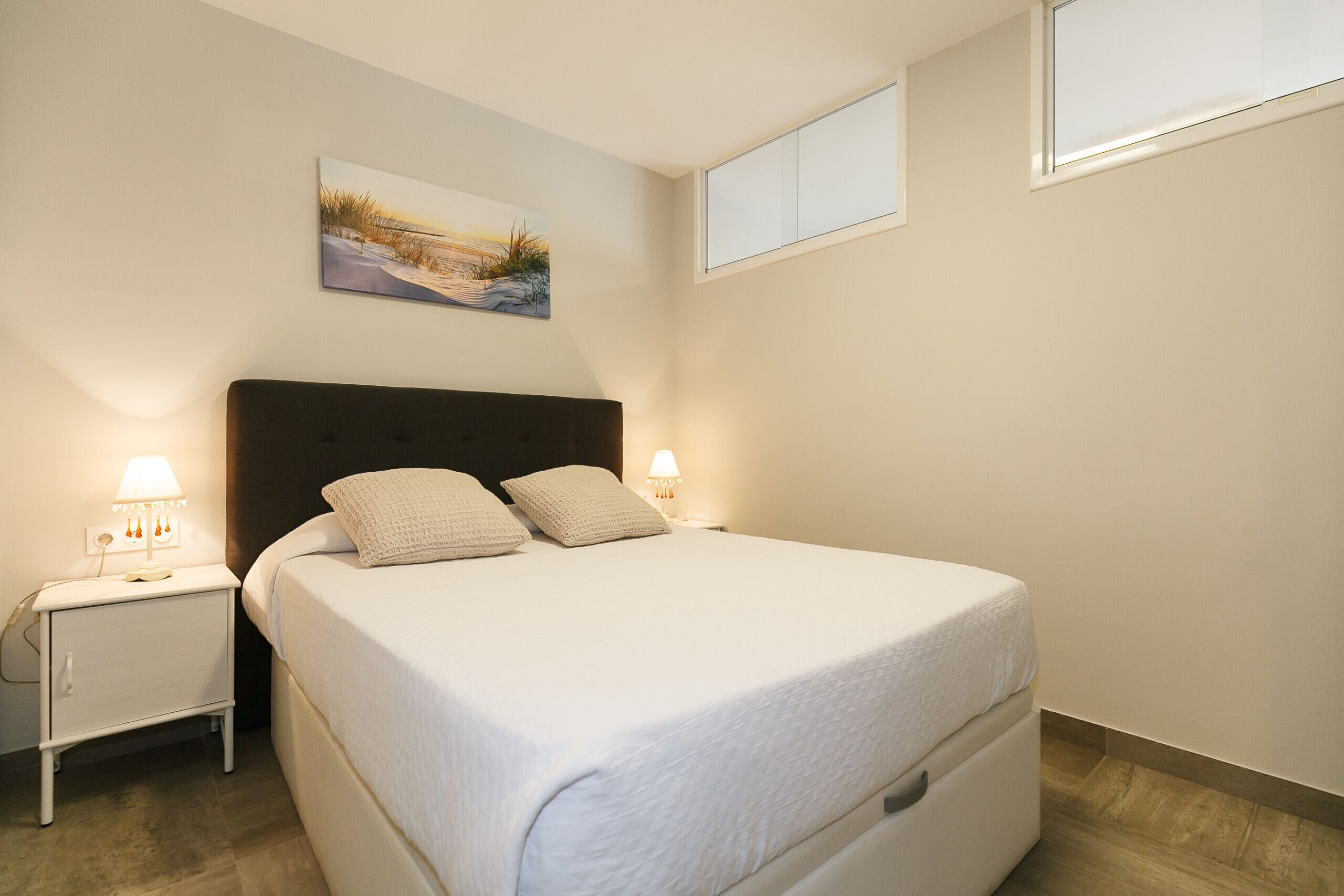 A neatly made bed with pillows, a bedside table with a lamp, and a painting on the wall.